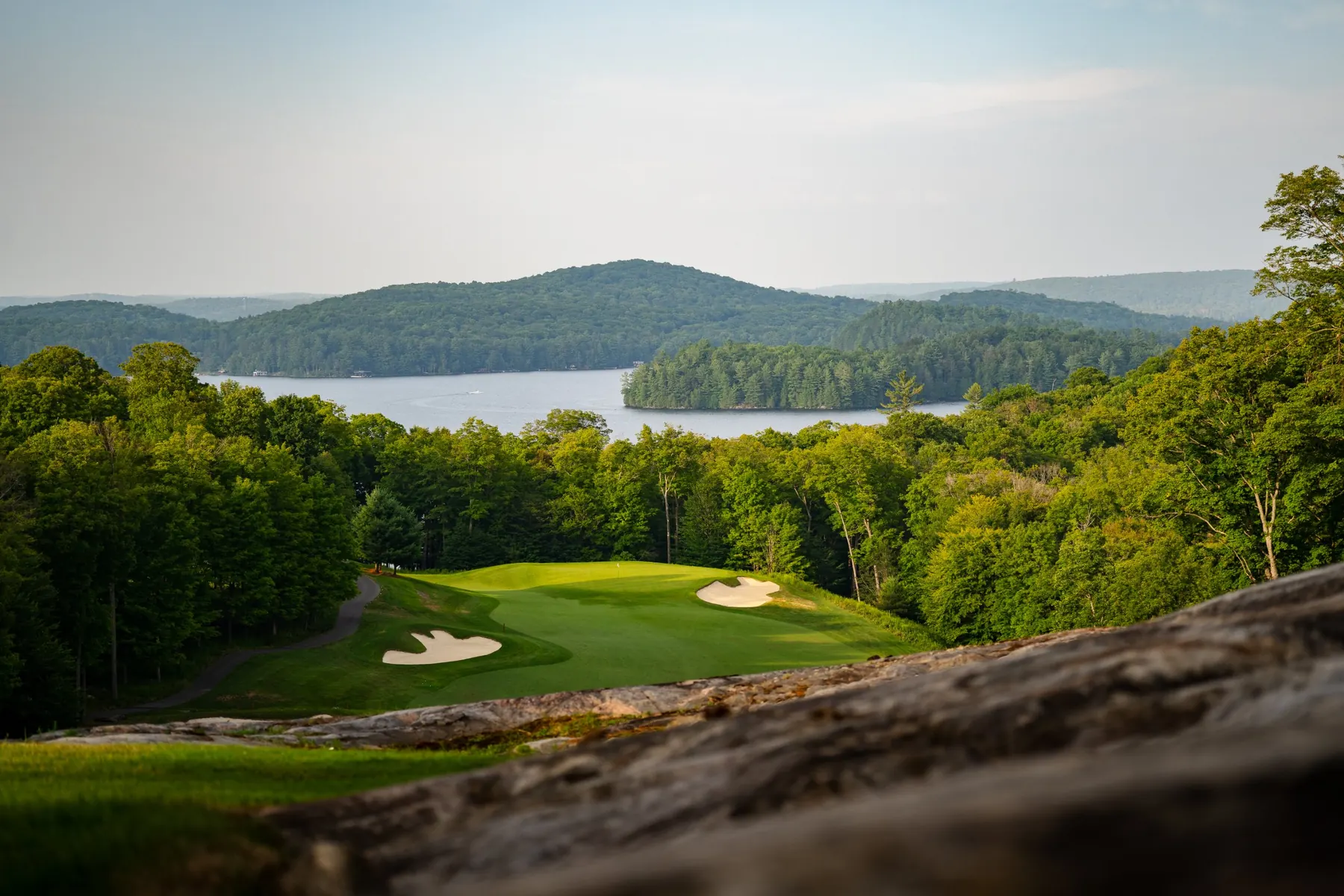 Looking over a rock outcrop to a green and Lake of Bays