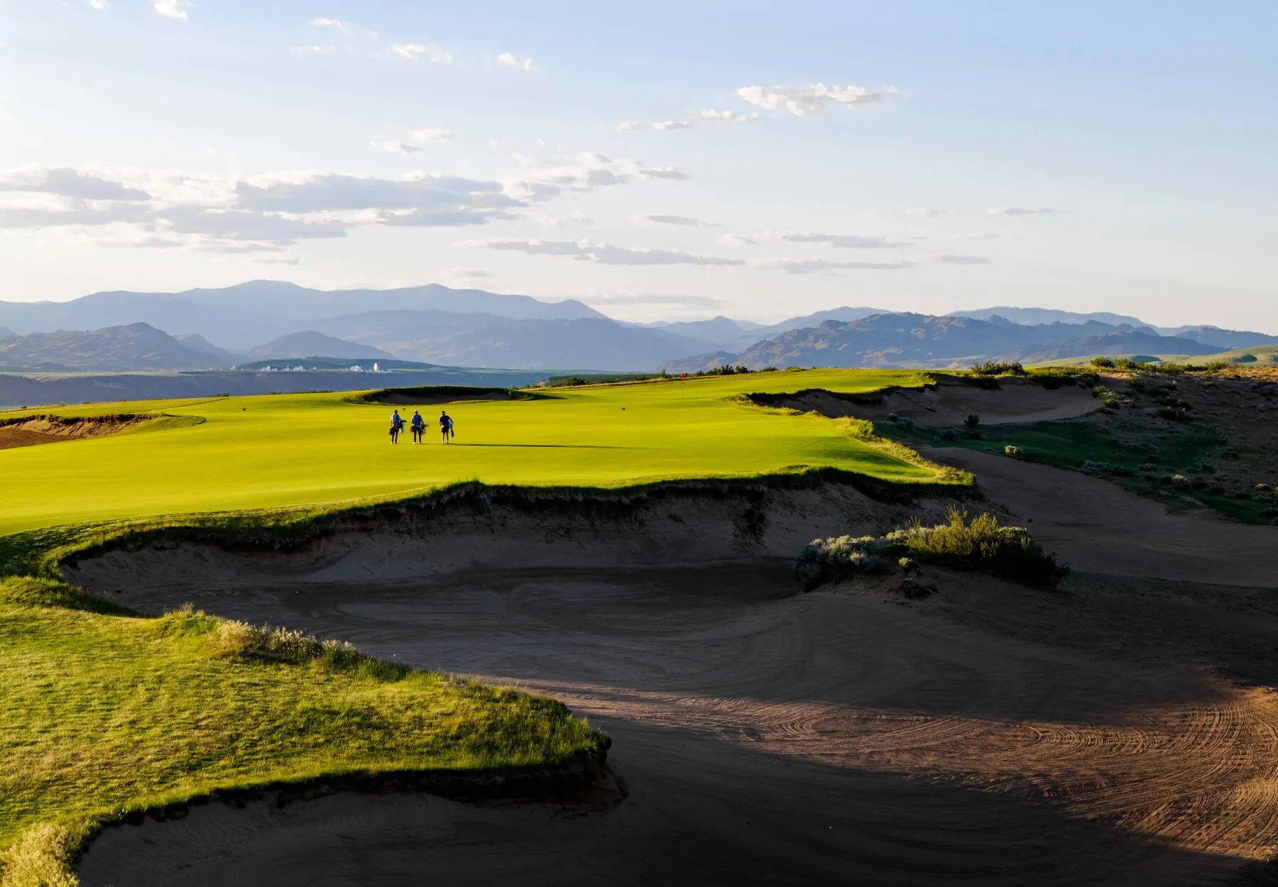 Golfers walking the fairway with mountains beyond