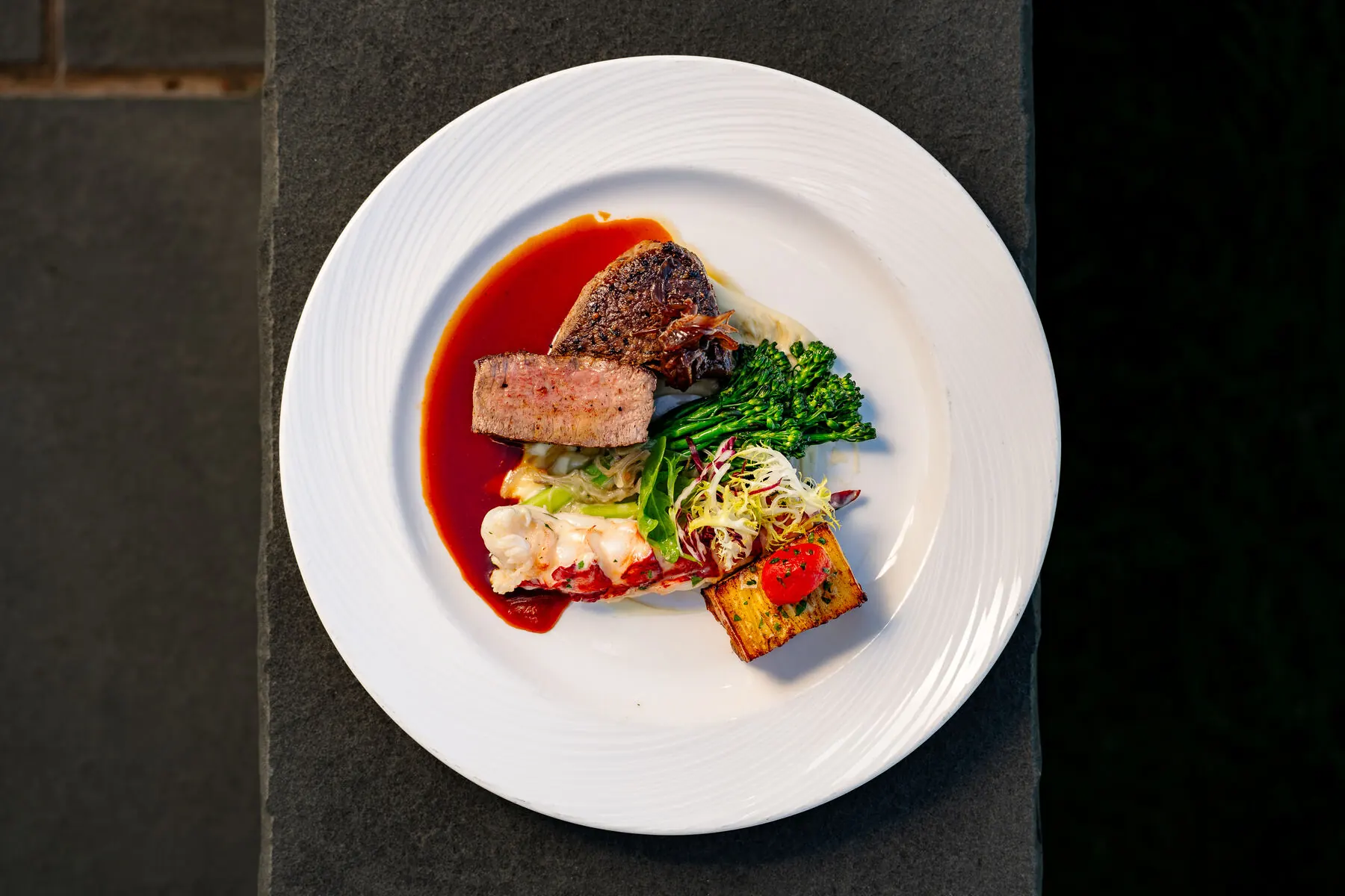 Plated steak, lobster, and broccolini at Huntington Crescent Club