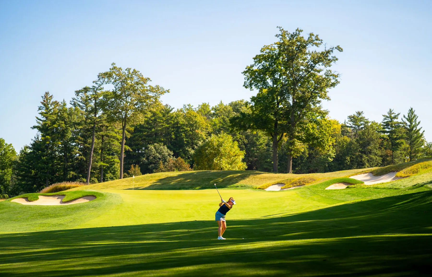 Golfer swinging toward the green flanked by bunkers